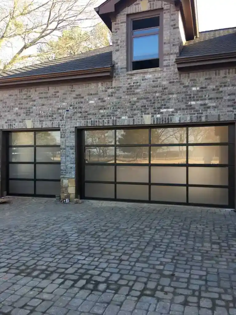 Double full view glass doors on brick home with paver driveway